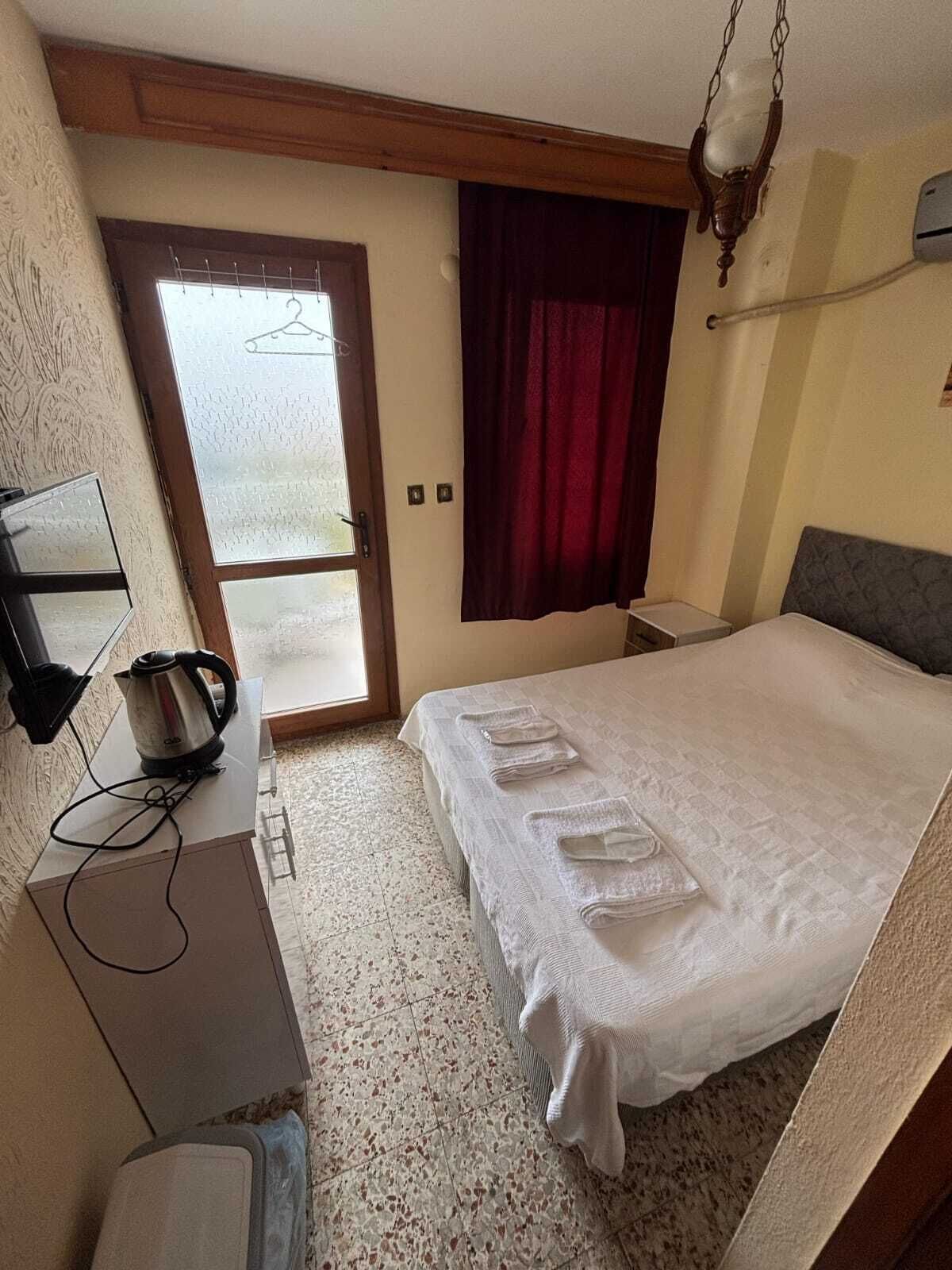 Een hotelkamer met een bed, een bureau met een waterkoker, een stoel, een klein tafeltje en een raam met uitzicht.