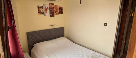 A hotel room with a bed, an air conditioning unit, a wall-mounted heater, and a door with a handle.