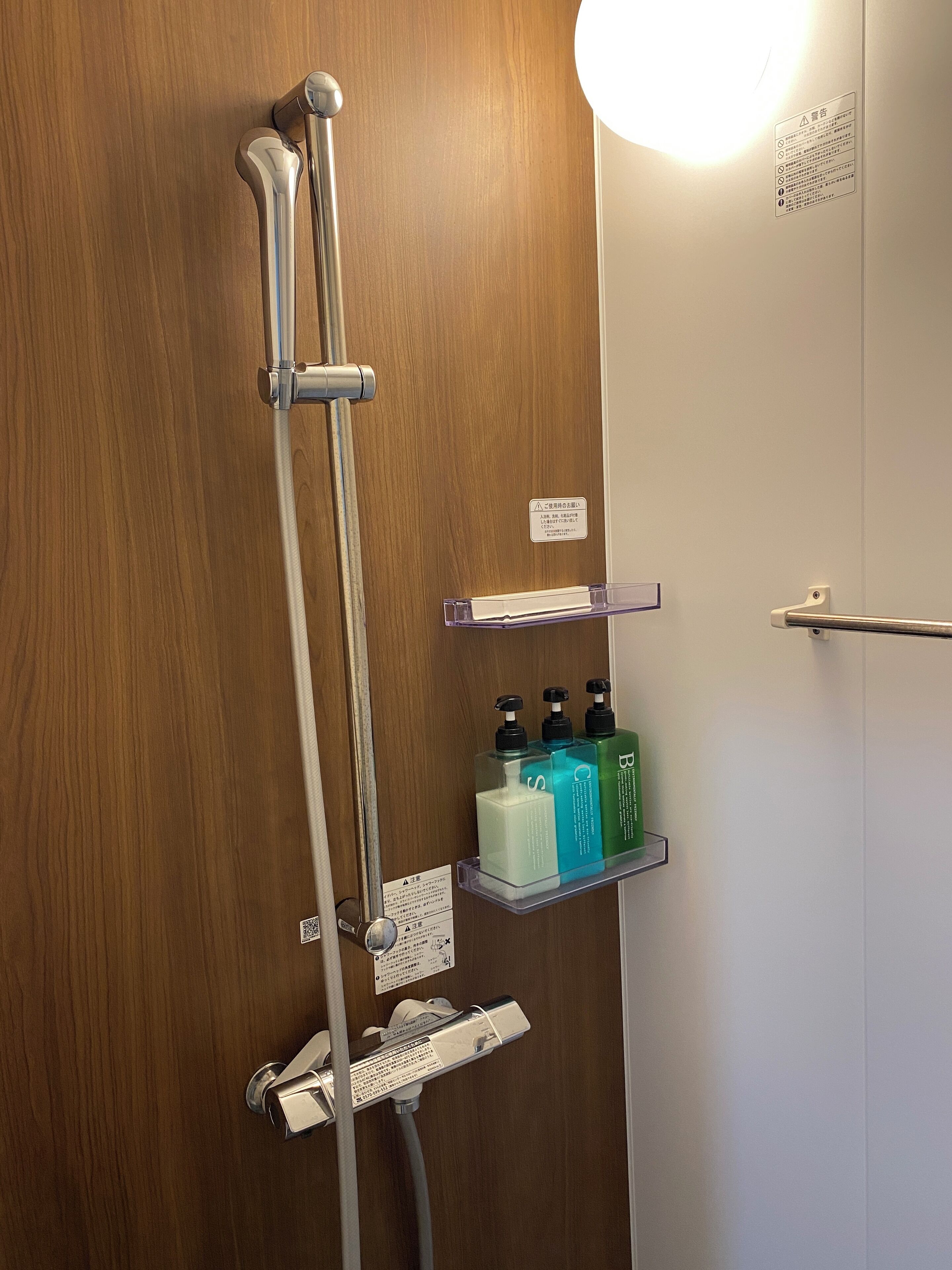 Puerta de madera con sistema de ducha, que incluye un cabezal de ducha manual y un grifo empotrado. Hay dos repisas con botellas de champú y acondicionador.