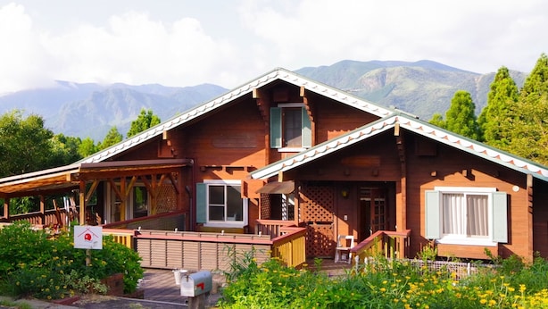 A wooden chalet with a sloped roof, a covered porch, and a view of mountains. - Private Room Guesthouse ORSA MINAMIASO (Minamiaso)