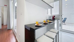 A modern kitchen with a black countertop, white bar stools, and a view of the snowy outdoors through the window. - Cityzen Funchal by Atlantic Holiday (Funchal)