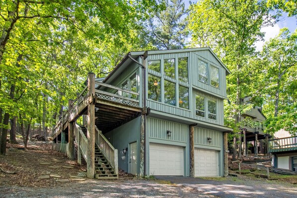A two-story wooden cabin with a garage, surrounded by trees.