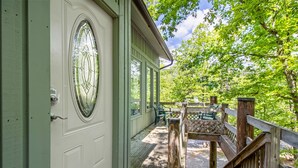 Una terraza de madera con baranda verde, una puerta blanca con ventana de vidrio y un pequeño espacio exterior con sillas.