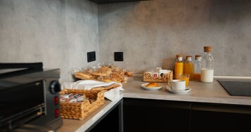 Preparación para el desayuno con pan, pasteles, jugo y leche sobre una encimera de cocina.