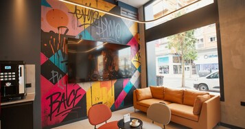 Un interior moderno con una pared llena de grafitis coloridos, un televisor de pantalla plana grande, un sofá de cuero y una cafetera.
