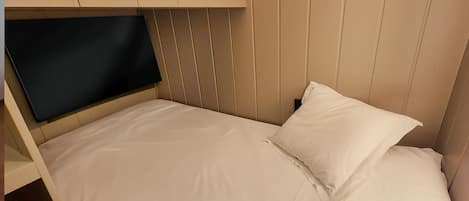 Una cama individual con cabecera, un televisor de pantalla plana montado encima y una almohada blanca.