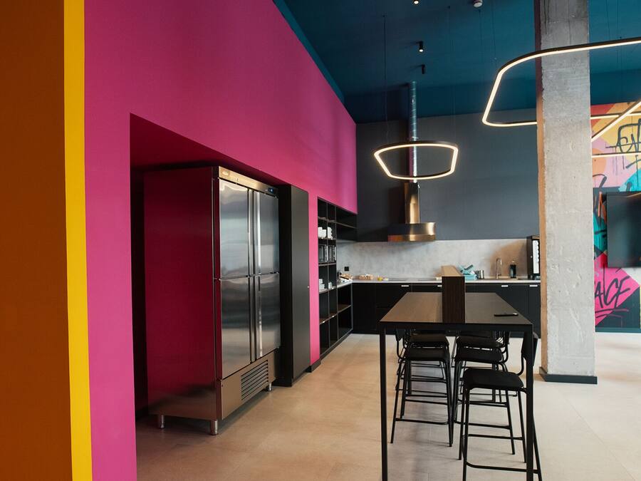 A modern kitchen with a large refrigerator, a dining area with stools, and a colorful wall with graffiti.