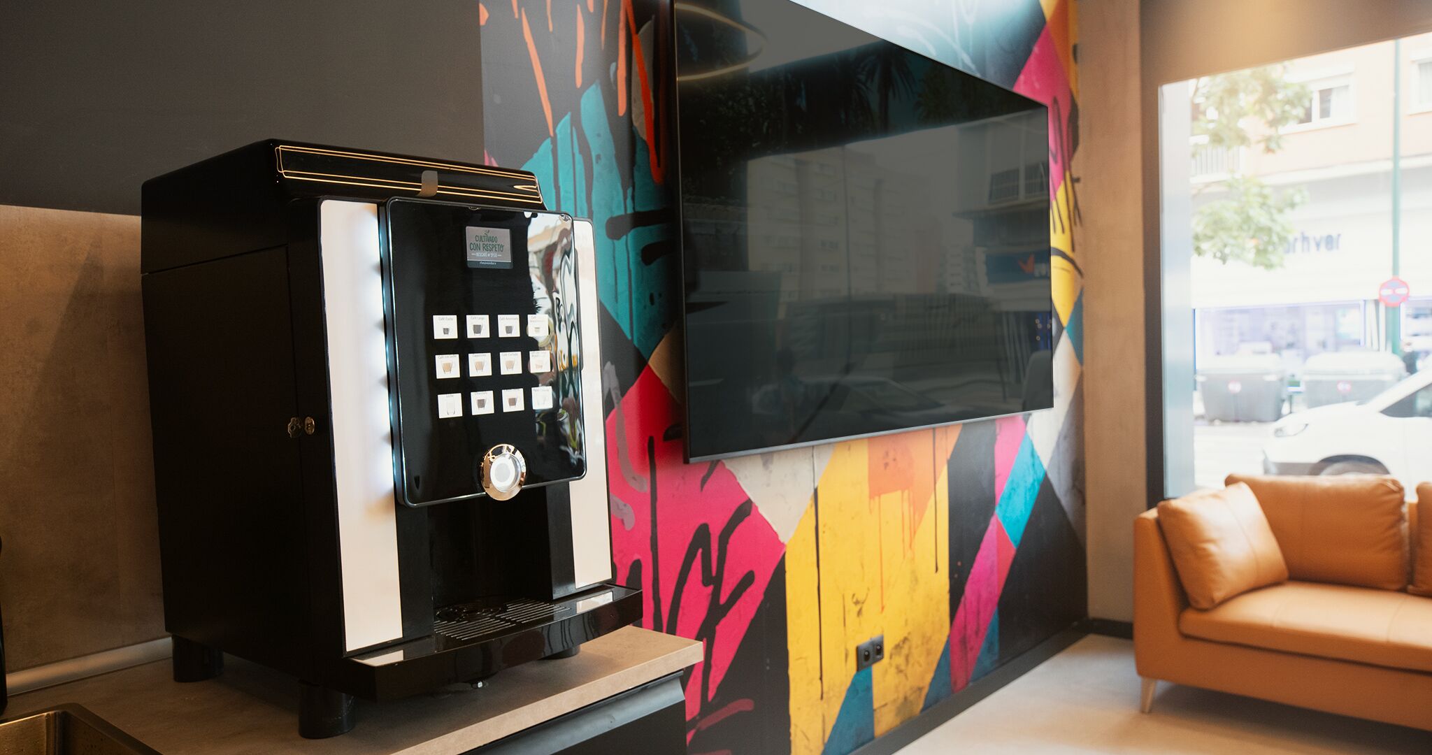 Una cafetera y un televisor de pantalla plana montado en una pared con un diseño geométrico colorido.