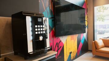 Una cafetera y un televisor de pantalla plana montado en una pared con un diseño geométrico colorido.