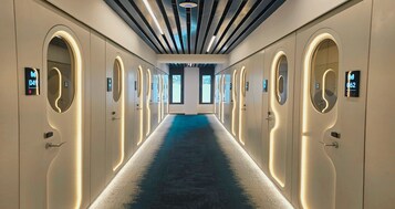 Un pasillo de hotel con alfombra azul, arcos y números iluminados que señalan los números de habitación.