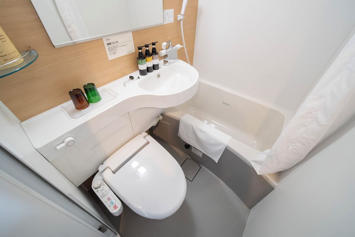 Une salle de bain moderne avec un lavabo, des toilettes et une baignoire blancs. On trouve des articles de toilette sur le comptoir du lavabo, et une serviette est accrochée à la baignoire.