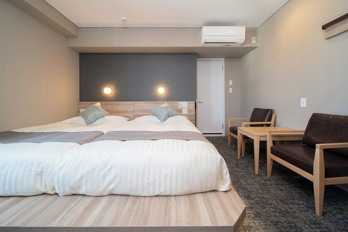 Une chambre d’hôtel moderne avec un grand lit, deux tables de chevet, une chaise et un appareil de climatisation.