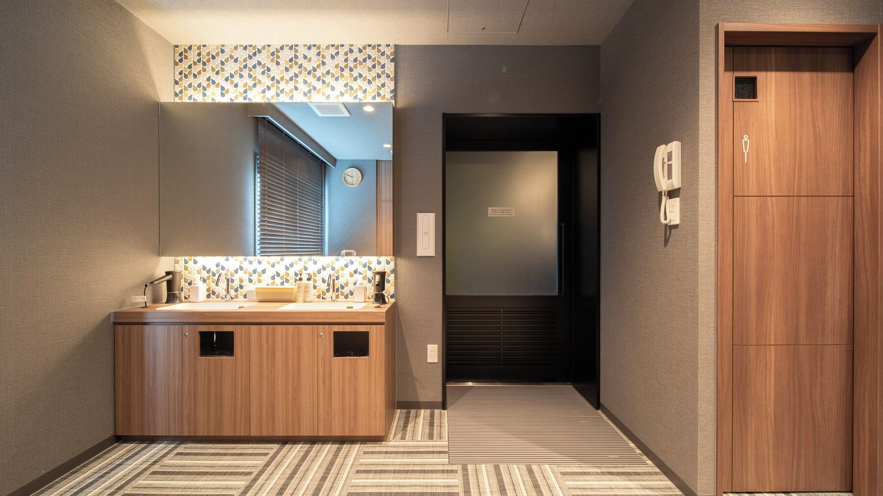 A modern bathroom with a wooden vanity, a mirror, and a patterned wall.