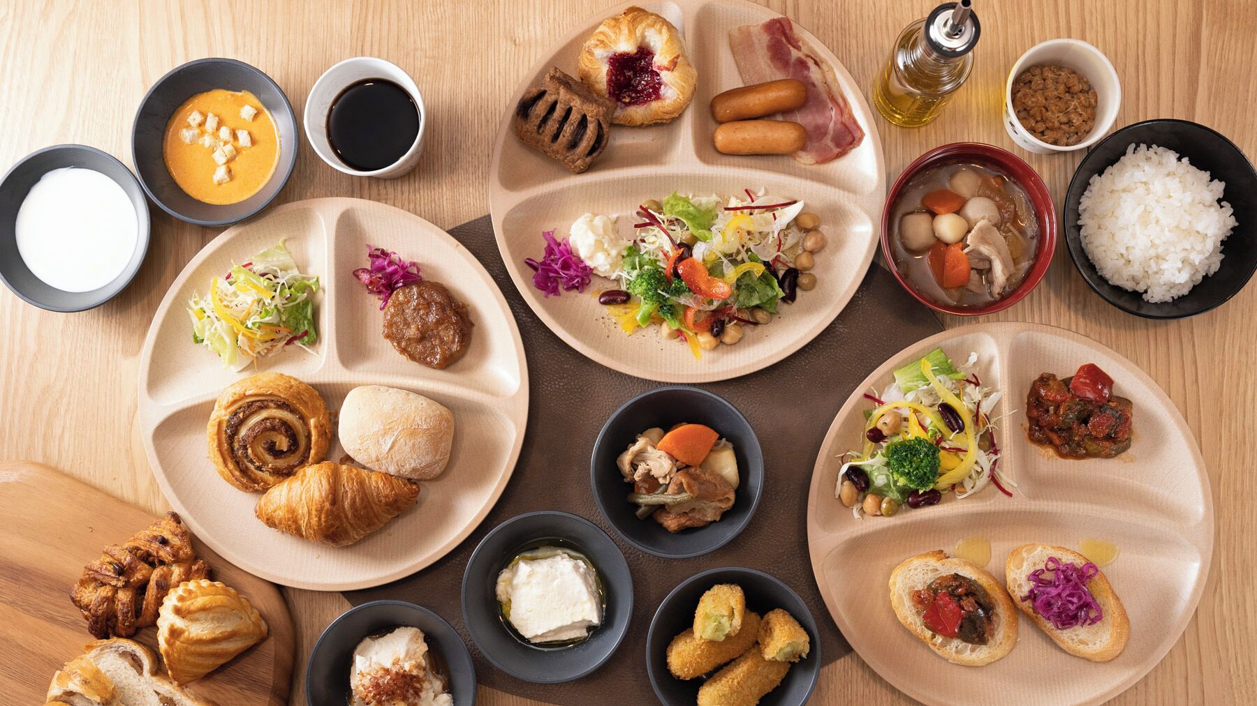 Diversos pratos com croissants, saladas e arroz, dispostos sobre uma mesa de madeira.
