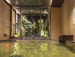 Un área de piscina interior moderna con paredes de vidrio transparente, un reloj digital y un banco.