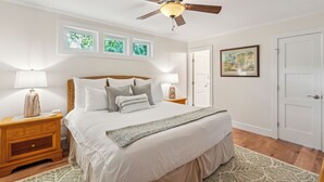 A bedroom with a bed, nightstands, a ceiling fan, a door, and windows. - Wild Dunes-Twin Oaks-Updated, sleeps 8, walk to beach and nearby shops! (Isle of Palms)