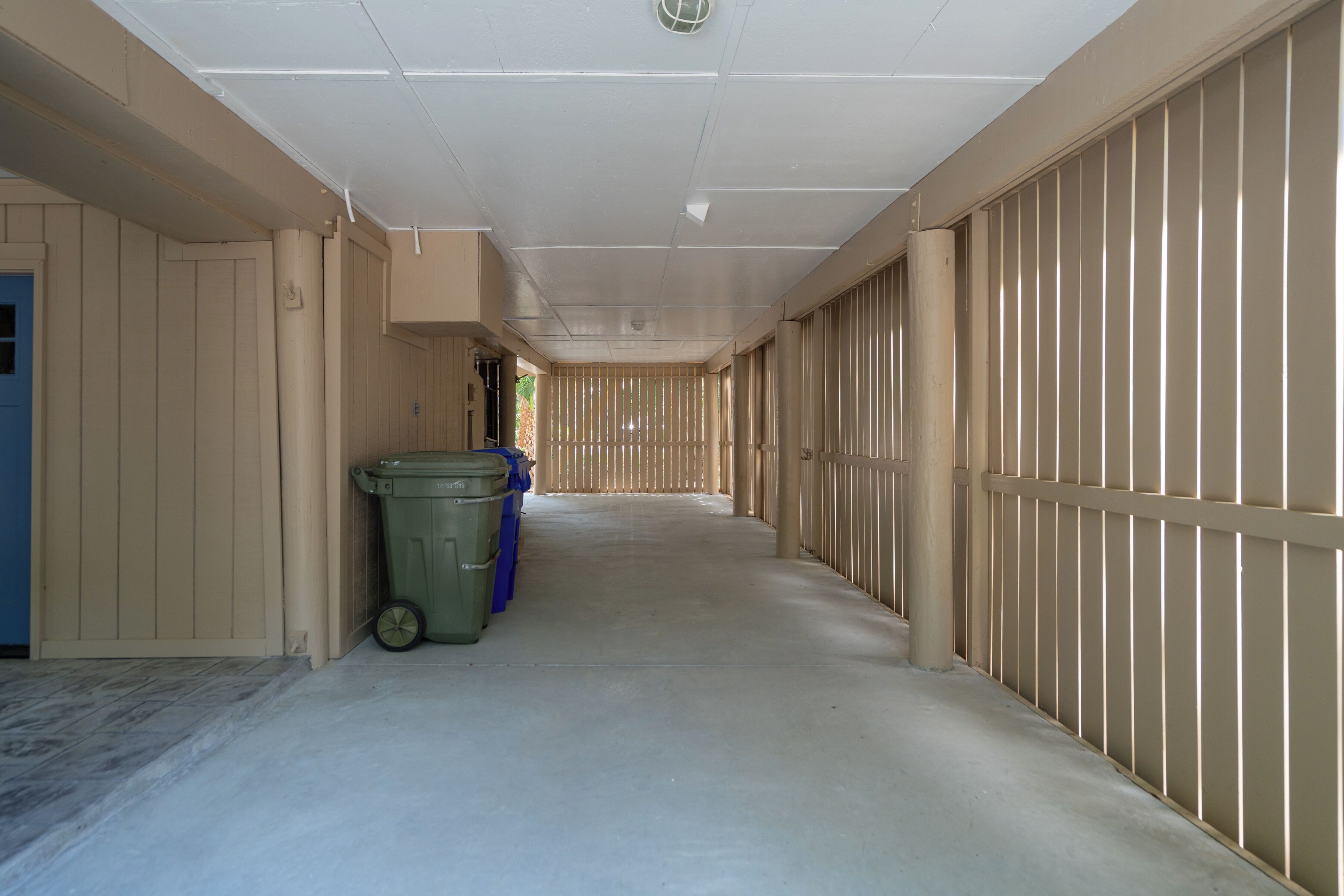 A corridor with beige walls and a tiled floor, leading to a door on the left.