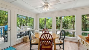 A dining area with a round table and four chairs, large windows with a view of trees, and a ceiling fan. - Wild Dunes-Twin Oaks-Updated, sleeps 8, walk to beach and nearby shops! (Isle of Palms)