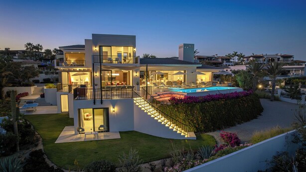 A modern multi-story house with a swimming pool, outdoor seating, and a well-lit staircase.