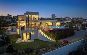 A modern multi-story house with a swimming pool, outdoor seating, and a well-lit staircase.