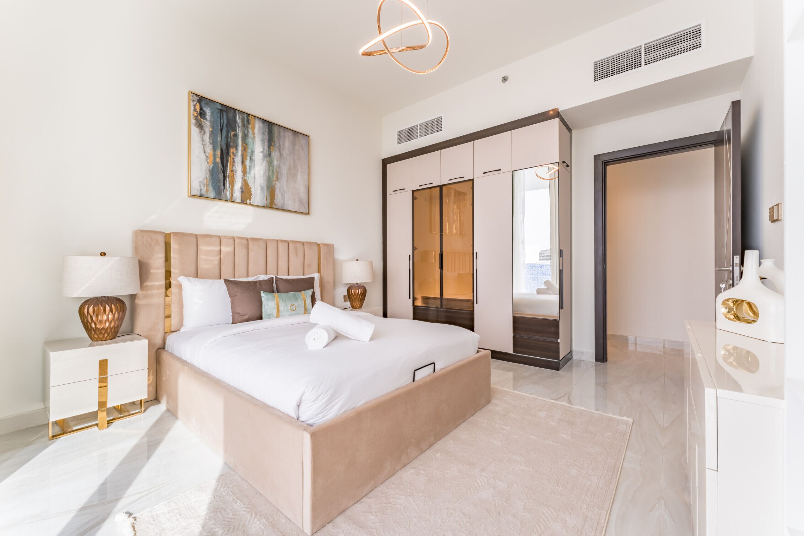 A modern hotel room with a large bed, bedside tables, a wardrobe, and a large mirror.