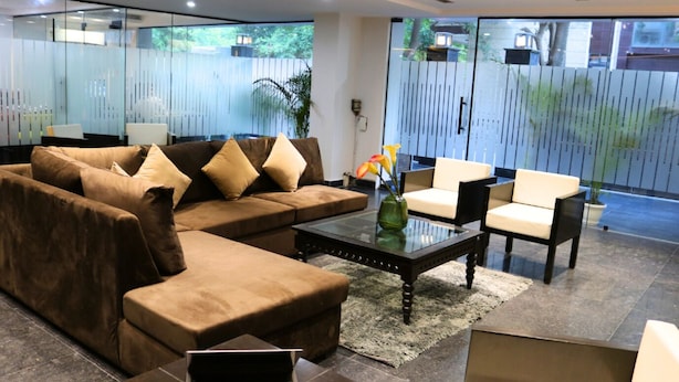 A modern living room with a sectional sofa, a glass coffee table, and a white armchair. - Fuji Ryokan Corporate Stays (Gurugram)