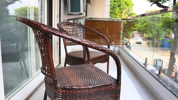 Dos sillas de mimbre en un balcón con vistas a una calle y árboles.