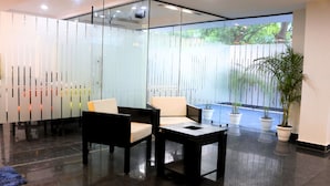 A modern reception area with glass partitions, a seating area with chairs and a table, and potted plants. - Fuji Ryokan Corporate Stays (Gurugram)