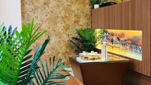 A modern lobby with a marble wall, a flat-screen TV mounted above a reception desk, and a large potted plant in the foreground. - Hello Banaras (Varanasi)