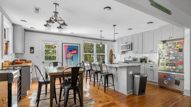 Una cocina moderna con armarios blancos, un refrigerador de acero inoxidable y un comedor con una mesa y sillas de madera.