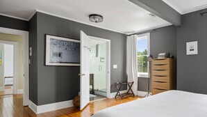 Un dormitorio moderno con una cama grande, un aparador de madera, un cuadro enmarcado en la pared y una puerta que da al baño.