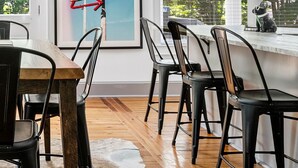 Una cocina moderna con zona de comedor, que incluye una mesa de madera, sillas negras y un ventanal con persianas.