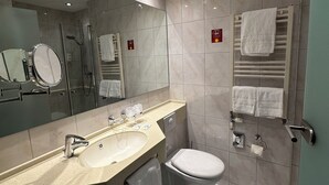 Ein modernes Badezimmer mit großem Spiegel, Waschbecken, Toilette und Duschbereich.