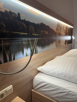 A hotel room with a bed, a nightstand, a wall-mounted lamp, and a large mural of a lake and trees. - Haven - Hotel Bochum (Bochum)