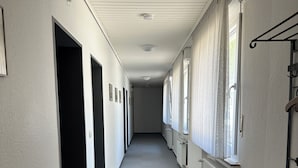 Ein langer, schmaler Korridor mit Teppichboden, weißen Wänden und einem Heizkörper an einer Seite.