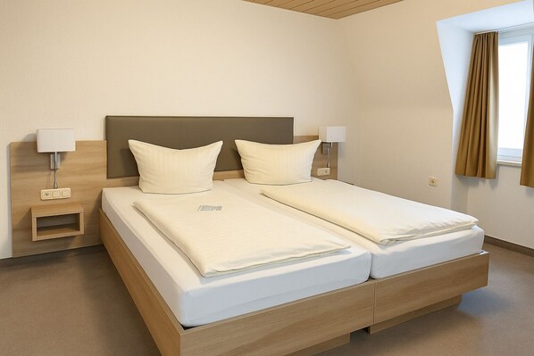 A double bed with a wooden headboard, two bedside tables with lamps, and a window with curtains. - Haven - Hotel Bochum (Bochum)