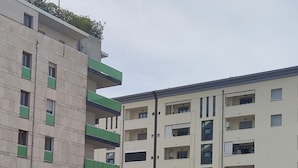 Ein mehrgeschossiges Wohngebäude mit Balkonen, einem Parkplatz und einem Ladenlokal.