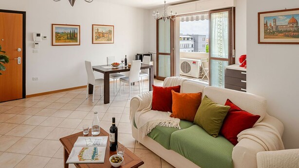 Ein Wohnzimmer mit Essbereich, einer Couch mit Kissen, einem Couchtisch mit Flasche und Gläsern sowie einem Gemälde an der Wand.