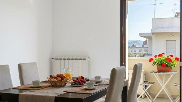 A balcony with a table set for breakfast, a radiator, and a view of buildings and mountains. - Modern & Bright •Free Private PArking!• Balcony • Close to City Center, 2BR+2BA (Firenze)