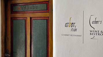 Een houten deur met een bord erboven en een muur met een logo en tekst die een restaurant met gastronomische keuken en een wijn- en bistro aangeven.