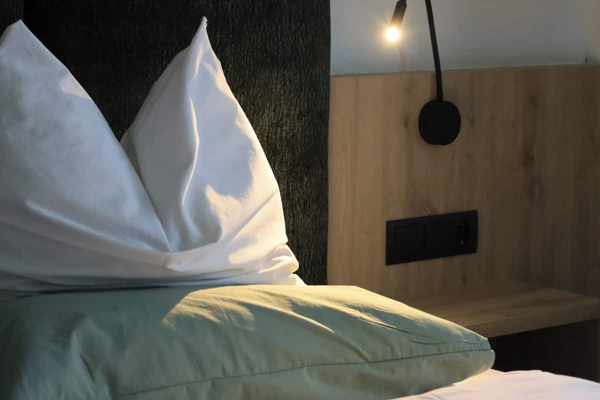 Una cama con almohadas, una lámpara fijada en la pared y un panel de madera.