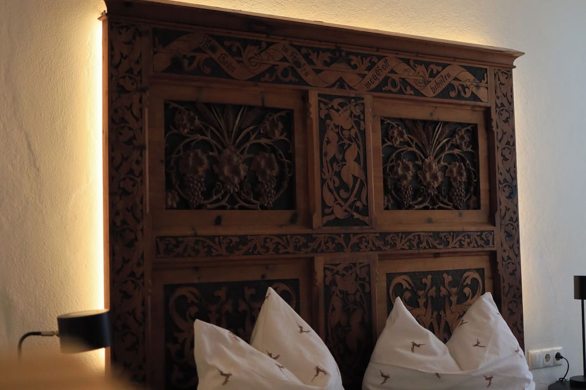 Un dormitorio con cabecera de madera, cama con ropa blanca y almohadas verdes, y mesita de noche con lámpara.