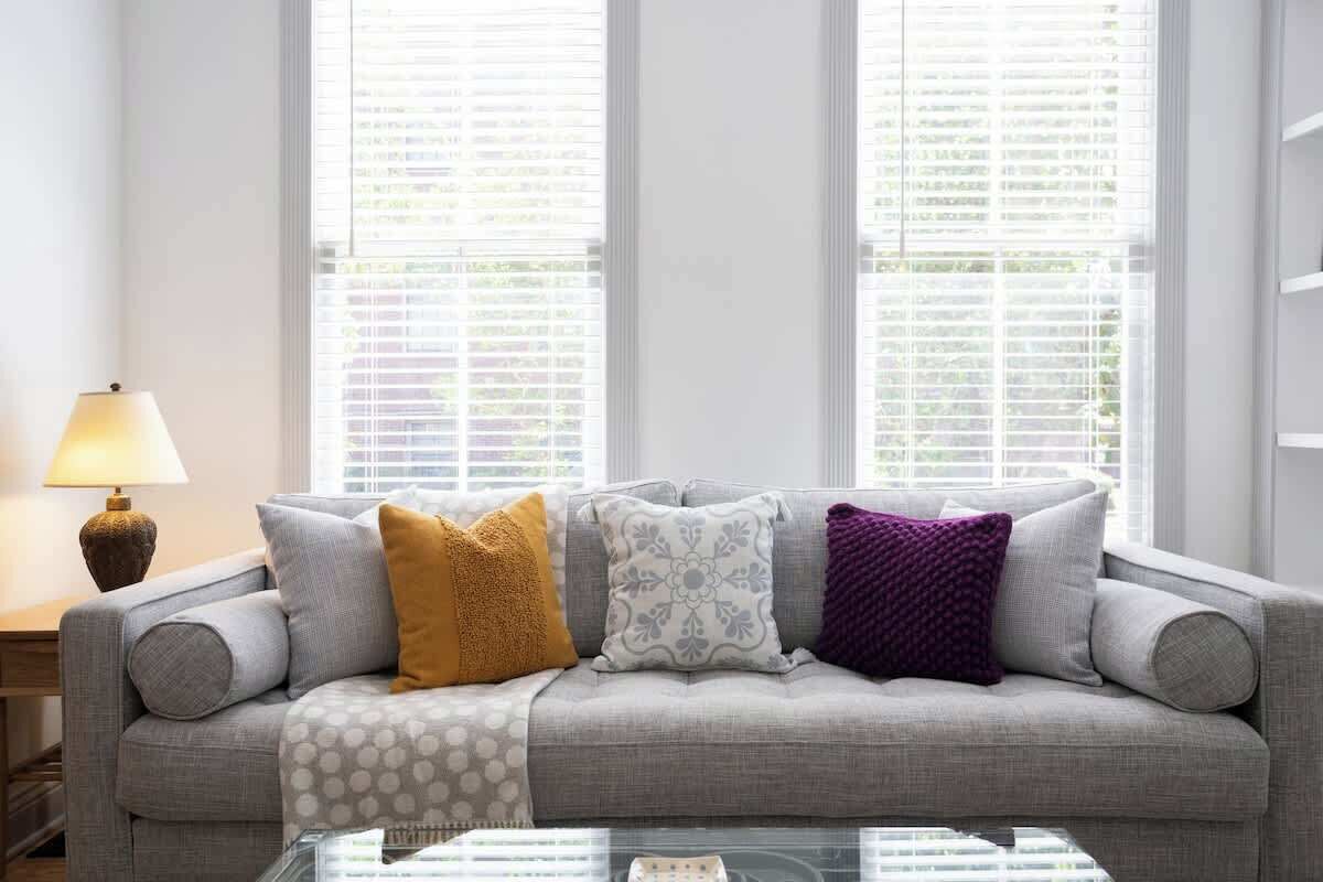 A grey sofa with patterned cushions, a glass coffee table, and a lamp on a wooden side table.