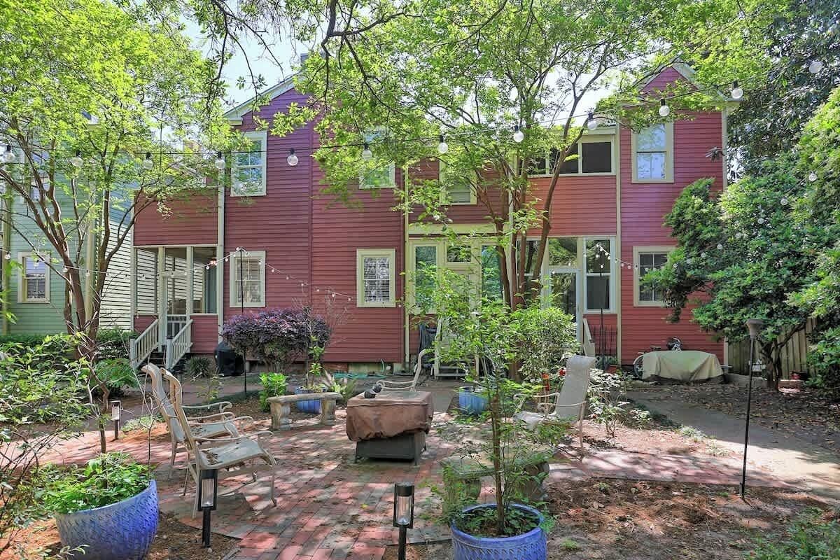 Ein rotes, zweistöckiges Haus mit einer Ziegelterrasse, Gartenmöbeln und Blumentöpfen.