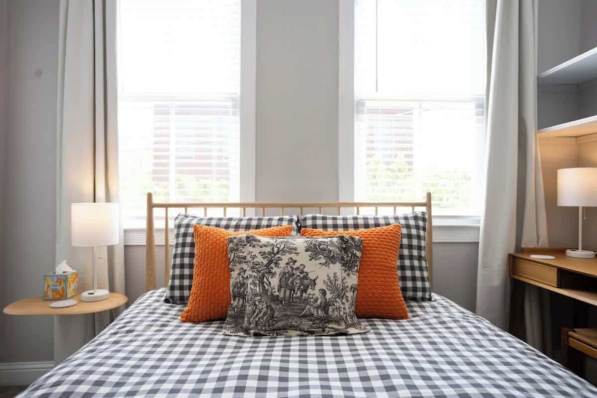 A neatly made bed with a checkered bedspread, two pillows, and a nightstand with a lamp and a tissue box.