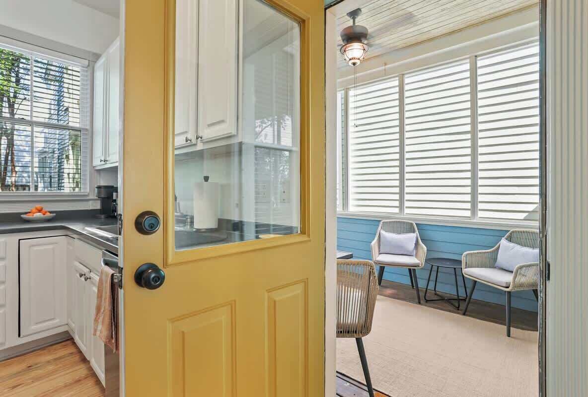A yellow door leading to a kitchen with white cabinets and a window with blinds.