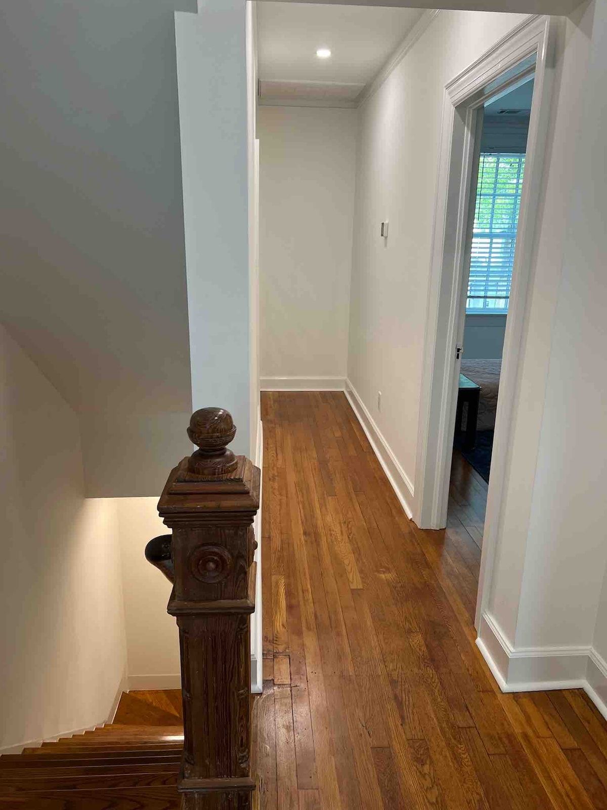 A hallway with wooden flooring, white walls, and a door leading to another room.