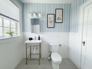Un baño con lavamanos, inodoro y decoración de pared a rayas.