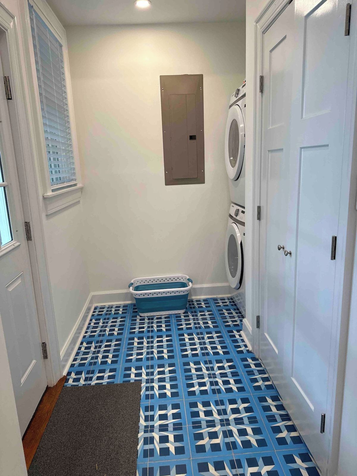 Une buanderie équipée d’un lave-linge, d’un sèche-linge et d’un panier à linge bleu, le tout posé sur un sol à motifs.