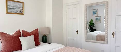 Un dormitorio ordenado con cama, almohadas, una lámpara de noche y un espejo.